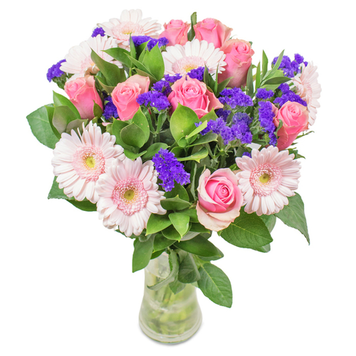 A carefully designed floral arrangement from Epsom, presented in a clear glass vase on a crisp white background. The display features seven to nine blush and medium pink roses, many petals just beginning to unfurl, reflecting classic spiral beauty. These rest alongside five to seven pale pink gerbera daisies, their generous, rounded petals radiating from soft, near-white centres, reminiscent of early blooms in Epsom's local parks. Vivid purple statice or limonium adds captivating texture and contrast, infusing the bouquet with depth and vivacity much like the bustling scenes of Epsom Market. Vibrant, lush green foliage forms a generous base, evoking the rich greenery found throughout the area's gardens and open spaces. Visible stems and fresh water within the transparent vase suggest recent harvesting and careful arrangement by local hands. Whether gifted for birthdays, anniversaries, Mother's Day, or shared as a decorative accent at home or work, this pink-and-purple bouquet embodies joy, celebration, and heartfelt affection-an elegant tribute to Epsom's blossoming character and community spirit.